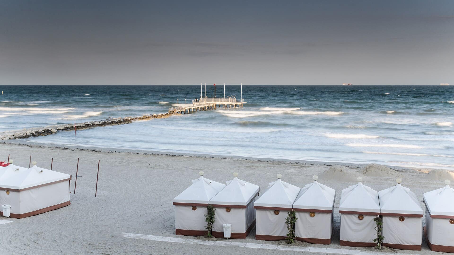 Eine Reihe weißer Strandkabinen im Sand vor der Adria am Lido di Venezia